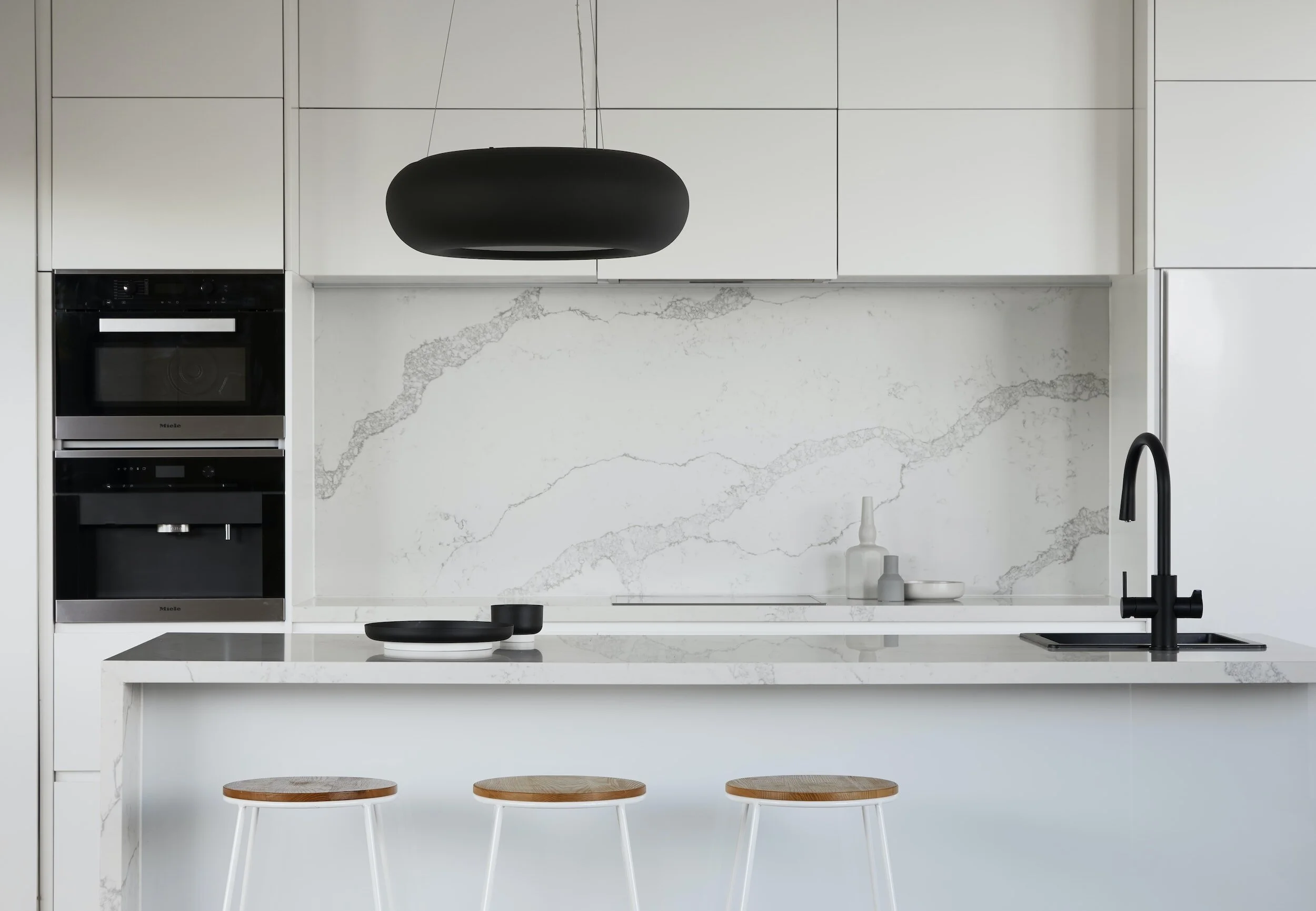 Minimalist Sydney kitchen featuring a full-height marble splashback, matte black tapware and a marble waterfall island