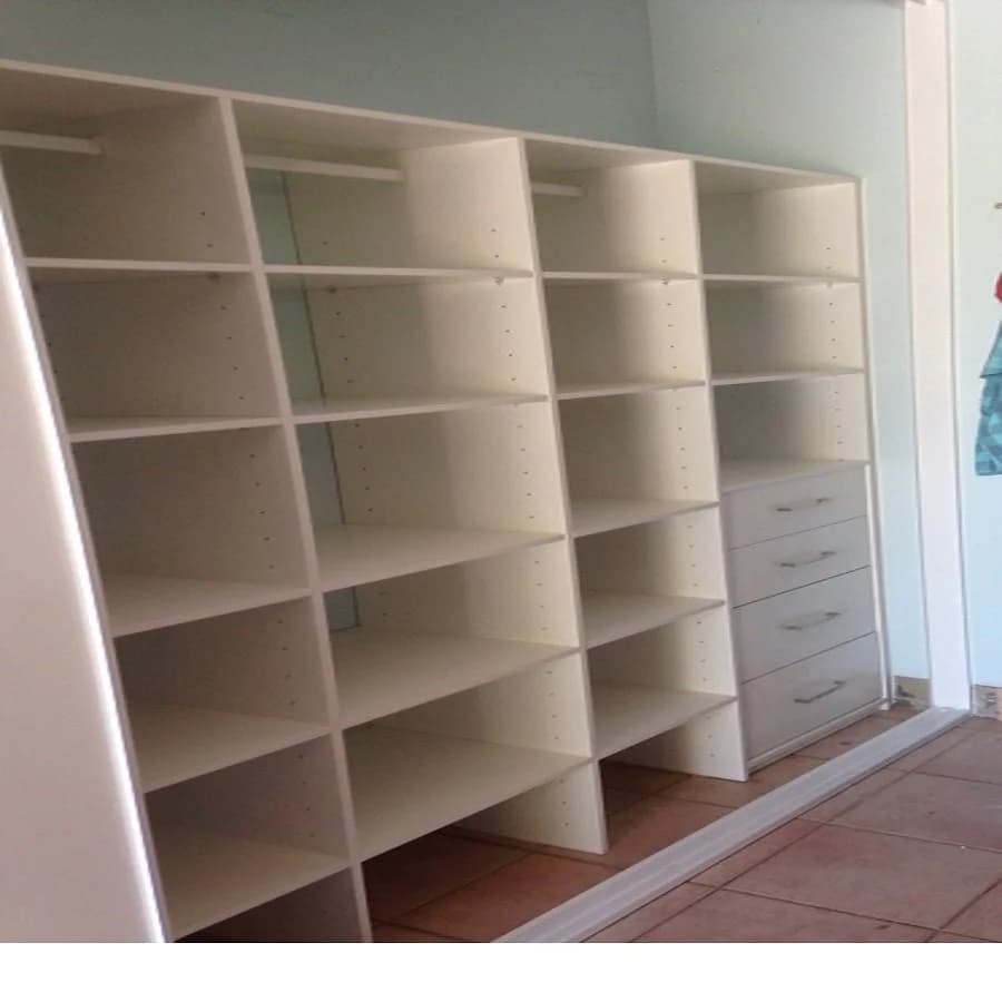 Seamless modern built-in wardrobe with floor-to-ceiling white panels and matte black handles in a sunlit bedroom